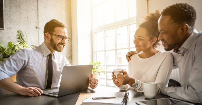 A husband putting his arm around his wife during a discussion with a credit union financial advisor sitting across from them.