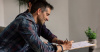 Two people sitting on a couch and looking at a document. One person has a pen in their hand and is signing the document.