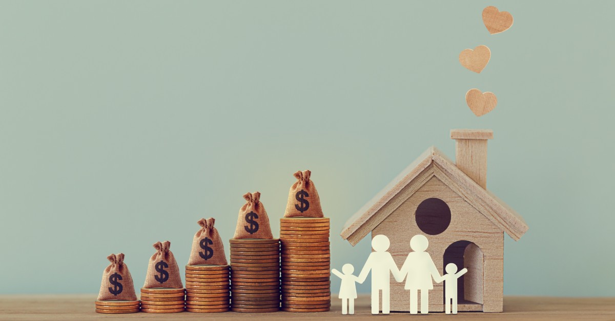 A set of pennies stacked together with small moneybags on top of them. There's a paper cut out of a family in front of a house.