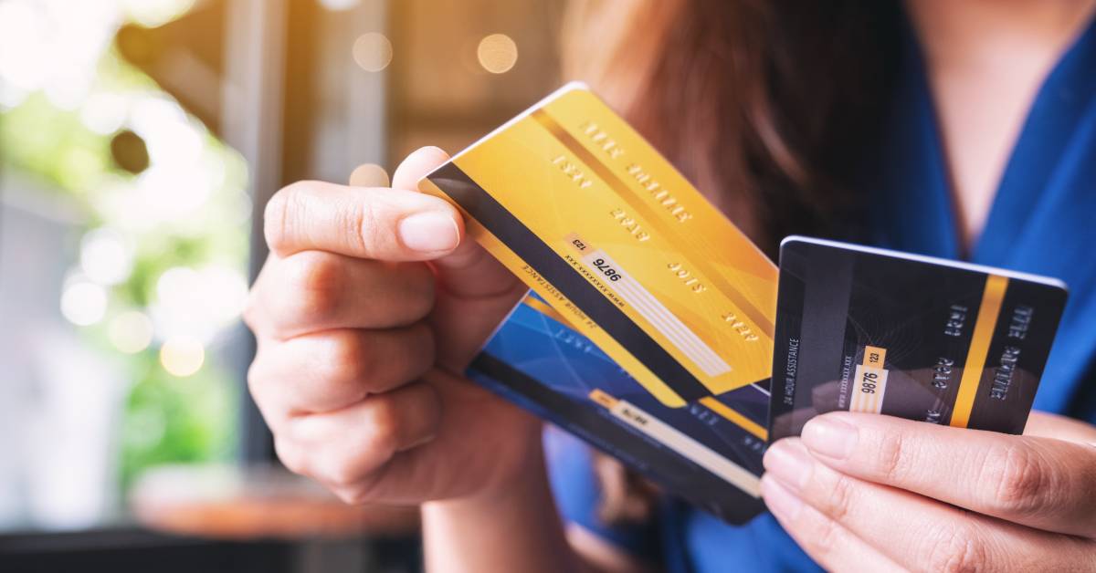 A woman holding three credit cards of different colors in one hand and pulling out one of them with the other hand.
